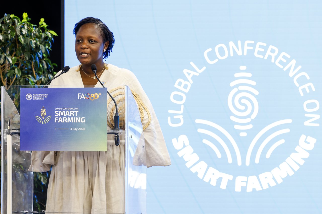 Chef Binta speaking at a lectern, with “Global Conference on Smart Farming” branding on the screen behind her.