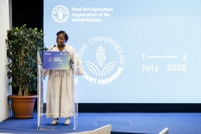 Chef Binta speaking at a lectern at a conference, audience seated in front of her.