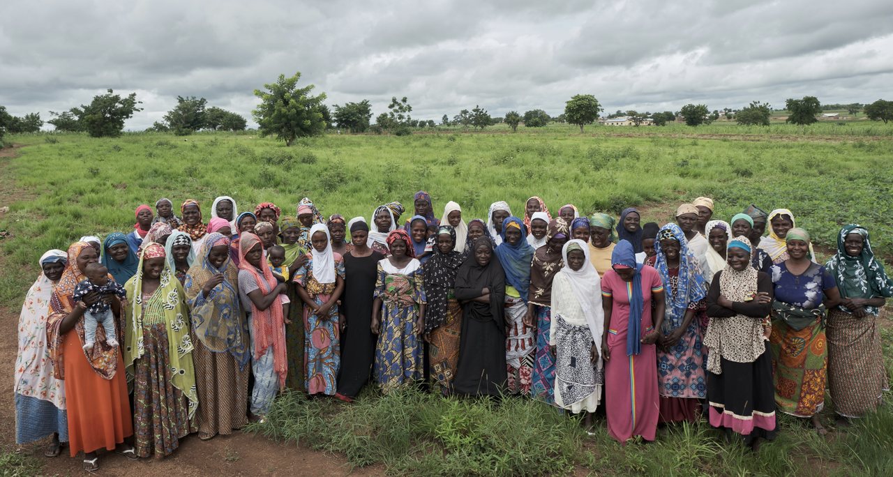 A large group of women stand together in a field, facing the camera.