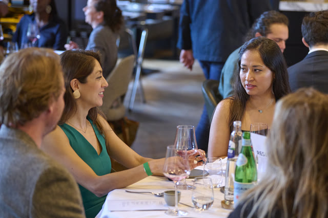 Guests seated at a long table in a restaurant dining room, mid-conversation.