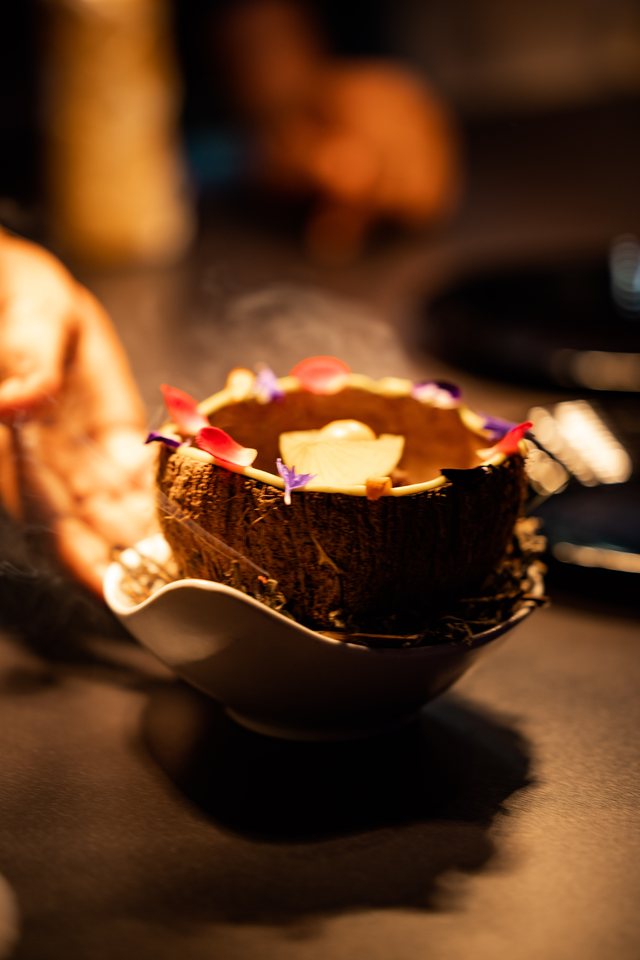 Close on hands holding a carved wooden bowl with a drink inside, warm evening light.