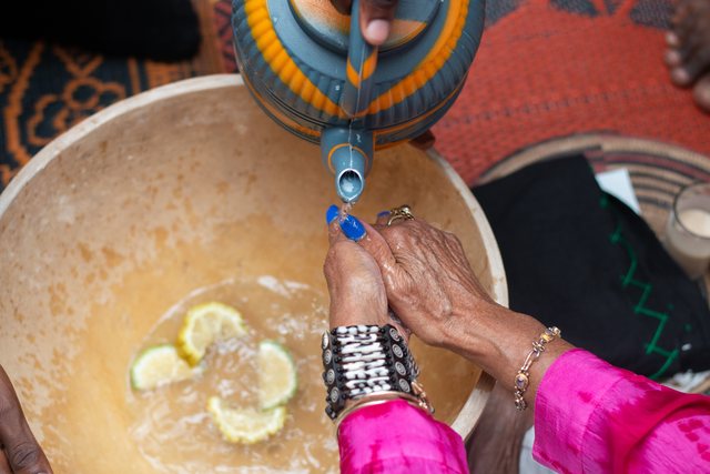 Hands squeezing a lime into a bowl, colorful clothing visible at the edges of the frame.