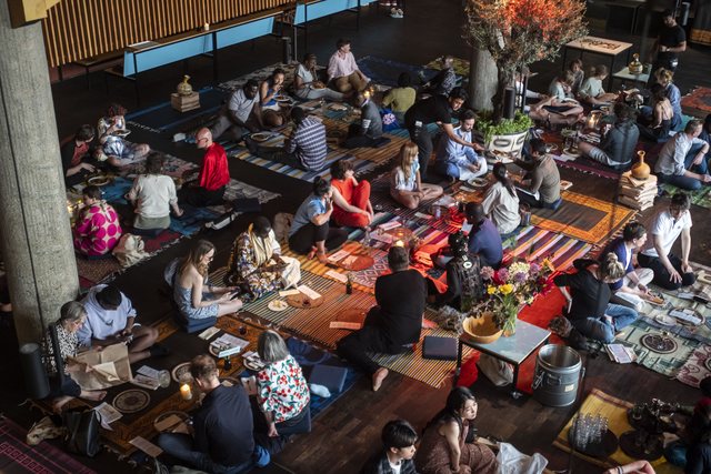 Looking straight down on a full Dine on a Mat dinner: guests seated in loose rows on mats, dishes laid between them, warm evening light.