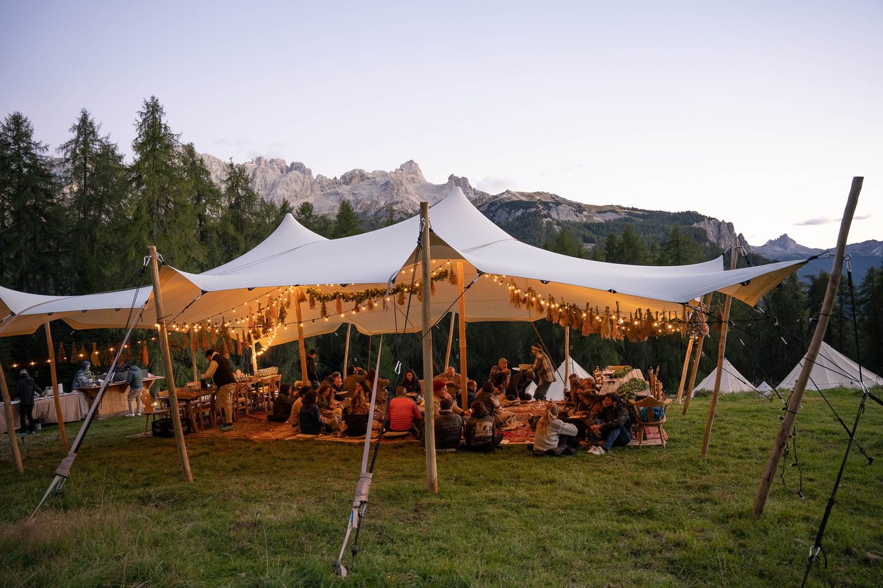 A white tented dining structure at dusk, string lights lit, mountains in the distance.