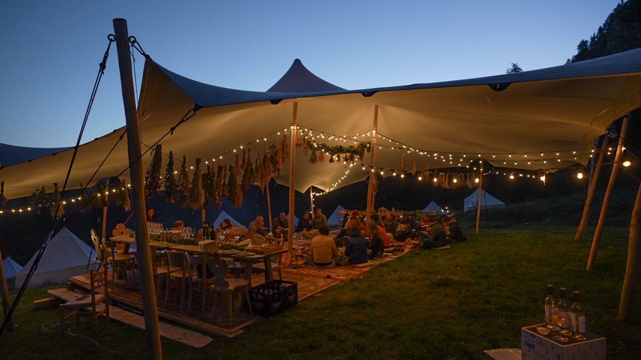 The white Dine on a Mat tent from further back, fully lit against the darkening sky.