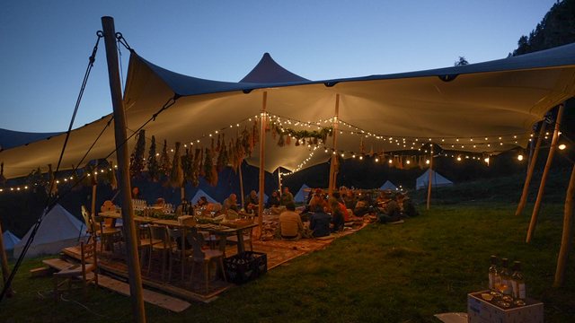 The same white tent from further back, fully lit against the darkening sky.