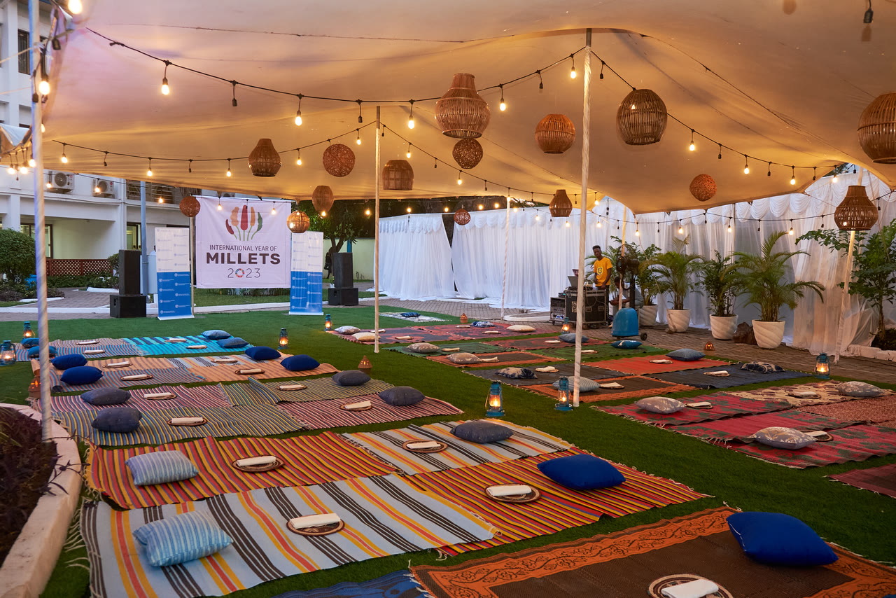 A tent laid with patterned rugs and low tables ahead of a dinner, a banner reading Millets visible at the back.
