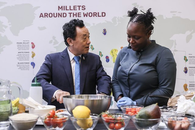 Chef Binta at a demonstration table branded “Millets Around the World,” cooking alongside another chef.