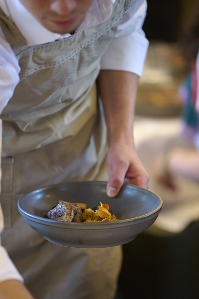 Close on a chef's hands plating a dish into a dark bowl.