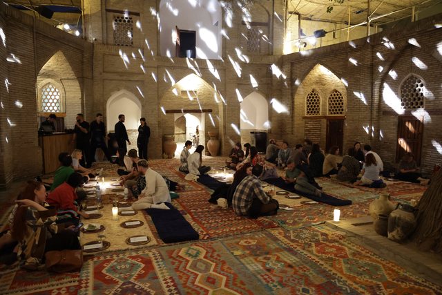 Looking up into an ornately domed room: star-shaped light falls through the ceiling onto guests seated on patterned rugs at low tables.